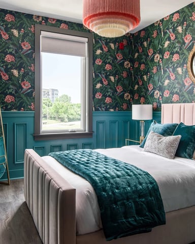 Bedroom with floral wallpaper, teal wainscoting, pink upholstered bed, and window overlooking trees