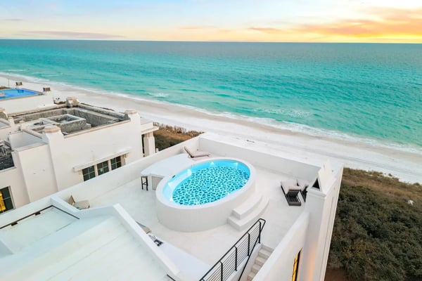 Modern white beachfront home with oval pool overlooking turquoise ocean and sandy beach at sunset