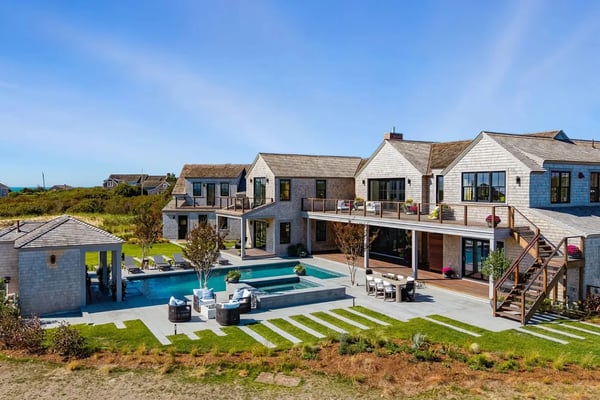 Modern white beachfront home with oval pool overlooking turquoise ocean and sandy beach at sunset
