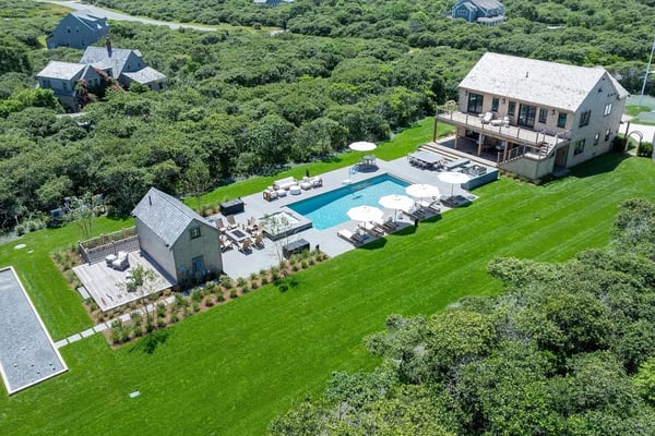 Modern three-story coastal home with metal roof, brick chimney, multiple decks, and backyard pool at sunset.